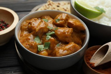 Lezzetli tavuk tikka masala, pilav, kişniş, kireç ve baharatlar ahşap masada, yakın plan.