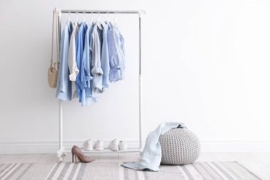 Askıda, çantada, ayakkabılarda ve beyaz duvarın yanında asılı farklı şık kıyafetler.