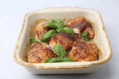 Lezzetli pişirilmiş tavuk butları ve fesleğen, açık gri masada, yakın plan.