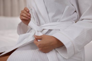 Kadın bornoz kemerini kapalı bir yerde yatağa bağlıyor, yakın plan.