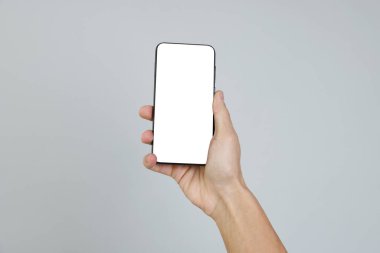 Gri arkaplanda boş ekranlı akıllı telefonu tutan adam, yakın plan.