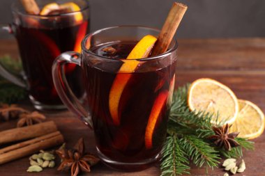 Lezzetli cam bardaklarda şarap, baharatlar ve köknar dalları ahşap masada gri arka planda, yakın planda.