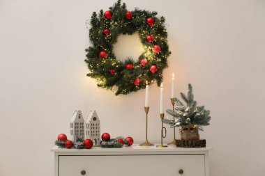 Beyaz duvarın yanındaki dolapta Noel süsleri ve yanan mumlar.