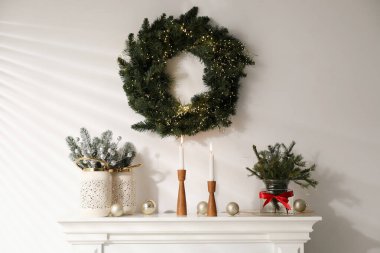 Beyaz duvarın yanındaki şöminede Noel süsü ve yanan mumlar.