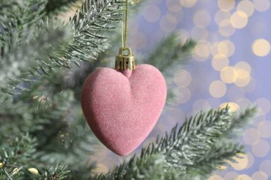 Noel ağacındaki kalp şeklindeki süs, arka plan rengine karşı bulanık ışıklar, yakın çekim ve yazı için boşluk. Bokeh etkisi