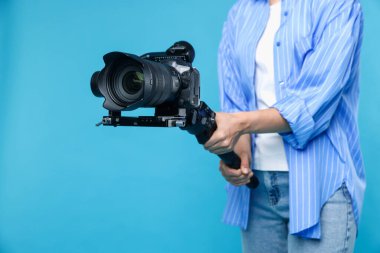 Açık mavi arkaplanda kamerası olan titreşimli dengeleyici kullanan kameraman, kapat