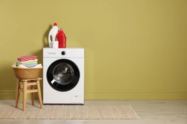 Modern çamaşır makinesi, deterjanlar ve zeytin duvarının yanındaki giysiler.