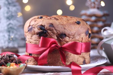 Masada kırmızı kurdeleyle süslenmiş, bulanık ışıklara karşı nefis bir Noel pastası, yakın plan. Bokeh etkisi
