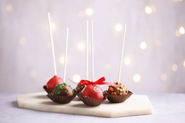 Tasty cake pops with sprinkles on grey table against blurred lights, closeup. Christmas snack