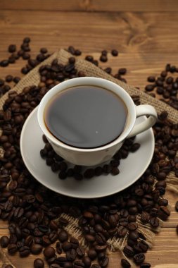 Aromatik kahve fincanda ve fasulyeler ahşap masada, yakın plan.