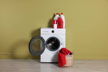 Modern çamaşır makinesi, deterjan ve zeytin duvarının yanındaki kıyafetler.