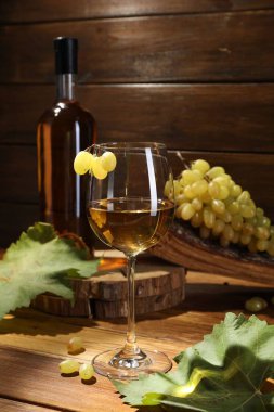 Lezzetli beyaz şarap, cam, şişe, üzüm ve yapraklar ahşap masada.