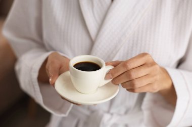 Bornozlu kadın, sabah kahvesi içeride, yakın plan.