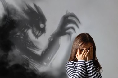 Korkmuş küçük kız gözlerini kapatıyor. Gri arka planda korkunç bir iblis. Fobi, patolojik korku.