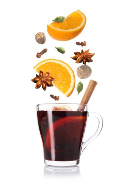 Sıcak şarap. Baharatlar ve portakal dilimleri beyaz arka planda cam bardak sıcak içeceğe dökülüyor.
