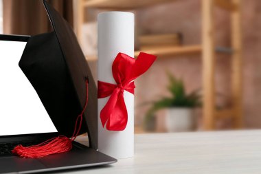 Diploma, mezuniyet şapkası ve beyaz ahşap masada dizüstü bilgisayar, yakın plan. Metin için boşluk