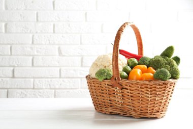 Tuğla duvara karşı beyaz ahşap masada hasır sepetteki farklı çiğ sebzeler.