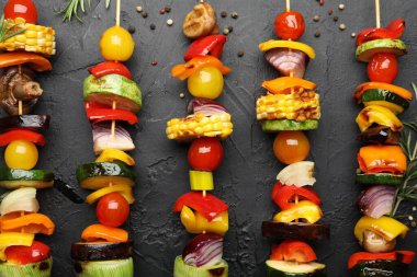 Skewers with tasty grilled vegetables on black table, flat lay