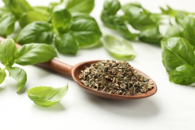 Kuru fesleğen yaprakları, taze olanlar ve kaşıklar ışık masasında, yakın plan.