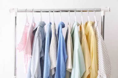 Beyaz duvarın yanında askıda asılı farklı şık kıyafetler, yakın plan.