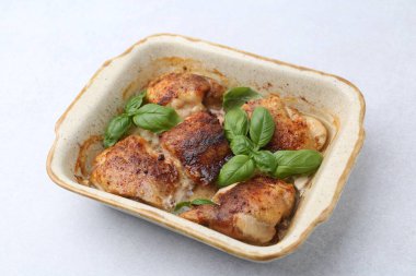 Lezzetli pişirilmiş tavuk butları ve fesleğen, açık gri masada, yakın plan.