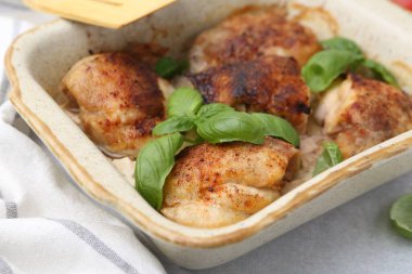 Lezzetli pişirilmiş tavuk butları ve fesleğen, açık gri masada, yakın plan.