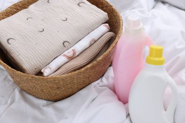 Çamaşır sepetinde katlanmış giysiler ve çarşafların üzerinde deterjan şişeleri, yakın plan.