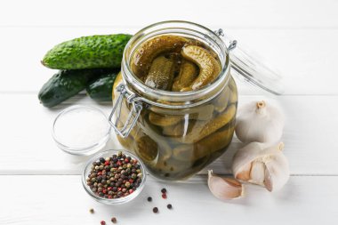 Kavanozda salatalık turşusu ve beyaz ahşap masada malzemeler, yakın plan.