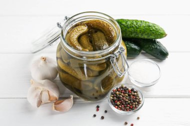 Kavanozda salatalık turşusu ve beyaz ahşap masada malzemeler, yakın plan.