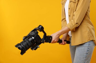 Kameraman sarı arka planda kameralı titreşim sabitleyici kullanıyor, yakın plan. Metin için boşluk