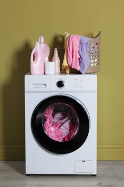 Modern çamaşır makinesi, deterjan ve zeytin duvarının yanındaki kıyafetler.