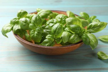 Açık mavi ahşap masada taze fesleğen yaprakları, yakın plan.