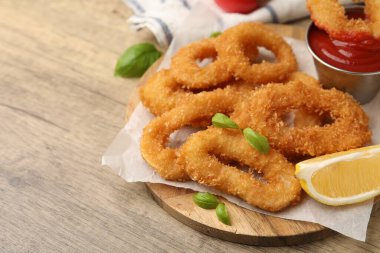 Limon dilimli kızarmış kalamar halkaları, ahşap masada fesleğen ve ketçap, yakın plan. Metin için boşluk