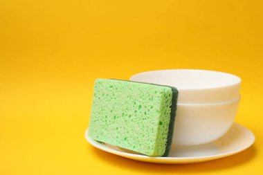 Mutfak süngeri ve sarı arka planda bulaşıklar, yakın plan. Metin için boşluk