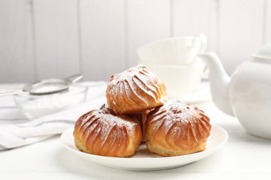 Beyaz ahşap masada servis edilen pudra şekerli lezzetli profiteroller.