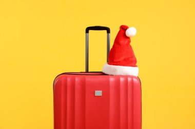 Kırmızı bavulda turuncu arka planda Noel Baba şapkası. Noel tatili