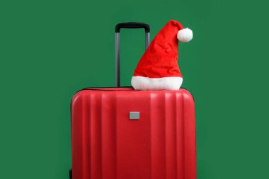 Kırmızı bavuldaki Noel Baba şapkası yeşil arka planda. Noel tatili