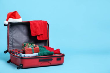 Noel tatili. İçinde Noel Baba şapkası, elbiseler ve açık mavi arka planda hediye kutuları olan bavulu aç. Metin için boşluk