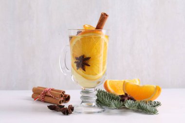 Cam bardakta baharatlı sıcak şarap, portakal dilimleri ve beyaz masada köknar dalları.