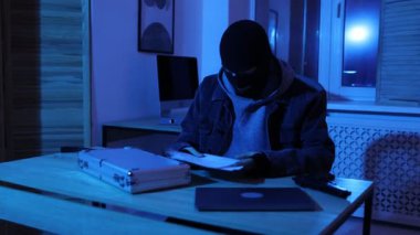 Maskeli bir hırsız gece ofiste para arıyor.