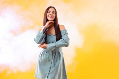 Turuncu arka planda poz veren güzel giyimli kadın dumanlı, mesaj için yer var.