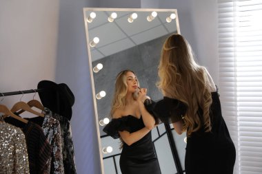 Güzel elbiseli çekici bir kadın aynanın yanında ruj sürüyor.