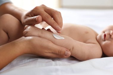 Anne evde bebeğinin koluna krem sürüyor, yakın plan.