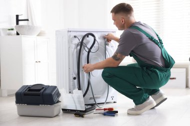 Üniformalı tamirci evde bozuk çamaşır makinesini tamir ediyor.