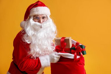 Sarı arka planda hediyelerle dolu çantalı Noel Baba, mesaj atmak için yer var. Mutlu Noeller ve mutlu yıllar.