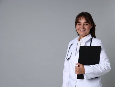 Stetoskop ve gri arka planda panosu olan tıp üniformalı bir doktor.