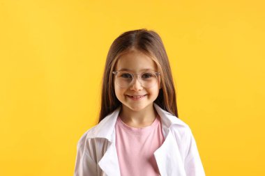 Sarı arka planda laboratuvar önlüklü ve gözlüklü gülümseyen küçük kız portresi. Çocuk ve bilim