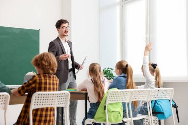 Çocuk sınıfta öğretmeninin sorusuna cevap vermek için elini kaldırıyor. Metin için boşluk