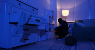 Maskeli hırsız içeride para arıyor.