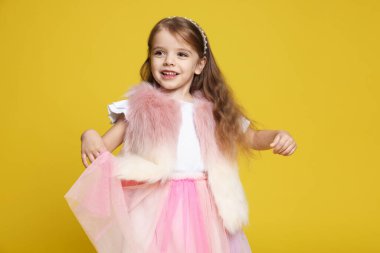 Sarı arka planda kürklü ve etekli mutlu küçük kız.